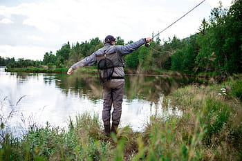 man, wearing, blue, holding, fishing rod, standing, green, grass, across, body, water