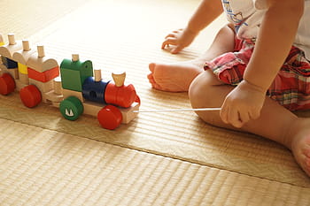 baby, wearing, white, shirt, holding, assorted-color, wooden, train toy, sitting, brown, flooring