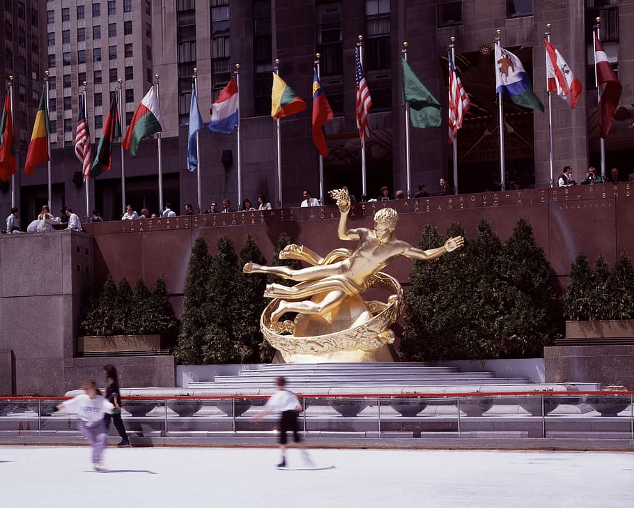 two, kid, skating, brass-colored statue, flags, daytime, new york city, rockefeller center, ice skating, rink, prometheus statue